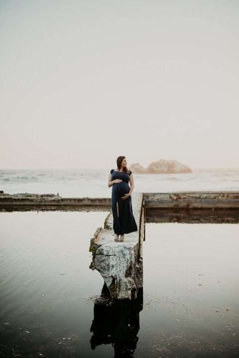 صورة لسيدة يبدو أنها حامل وتقف على حافة بحيرة وقت الغروب وتنظر على يسترها. وتبدو الصورة هادئة وتدعو للسكينة والهدوء.